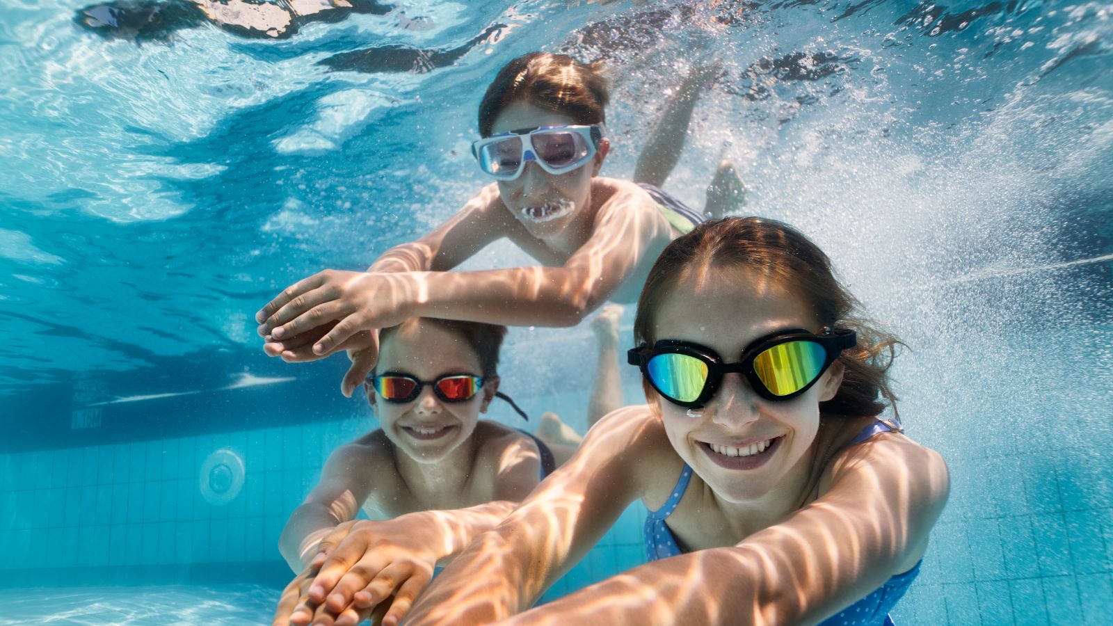 Smiling kids wearing goggles underwater in a swimming pool